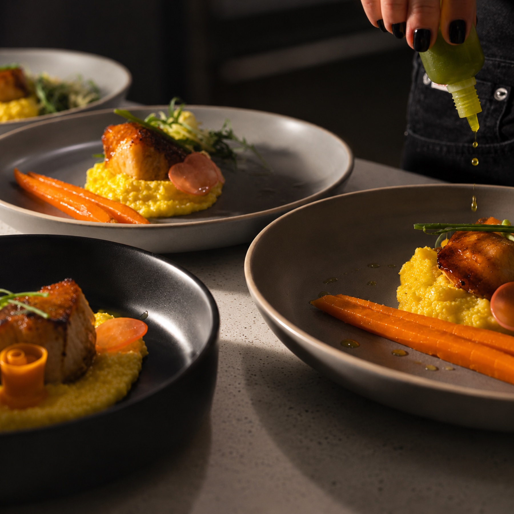 Salmon over saffron polenta with roasted carrots, chef drizzling herb oil